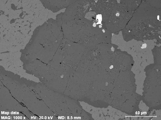 Plagioclase and K-feldspar in a granite from Maine. In the backscattered electron image the large gray crystal in the middle is intermediate plagioclase. It has a thin, darker-gray albite rim, which is the last plagioclase to crystallize. The lighter gray phase is K-feldspar, which has abundant dark-gray albite exsolution blobs. Some of the albite rim on plagioclase is exsolved from the K-feldspar. The light-gray phase is apatite, and white is magnetite and zircon. In the X-ray map (put cursor over the image) the zoning from Ca-rich core to Na-rich rim of the plagioclase is obvious. The K-feldspar is green, apatite yellow, and magnetite red. Note that the plagioclase also has K-feldspar inclusions.
