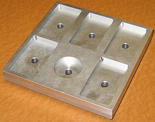 This is another specially designed sample holder built for the Geology Department. It accepts five polished petrographic thin sections (27 x 46 mm) and one 25 mm diameter standard block. Flanges inside the holes keep all specimens coplanar. This also has a faraday cup. The bolts that hold the top and bottom halves are on the back. Put cut pieces of soda straws to push thin sections and the standard block against the flanges.